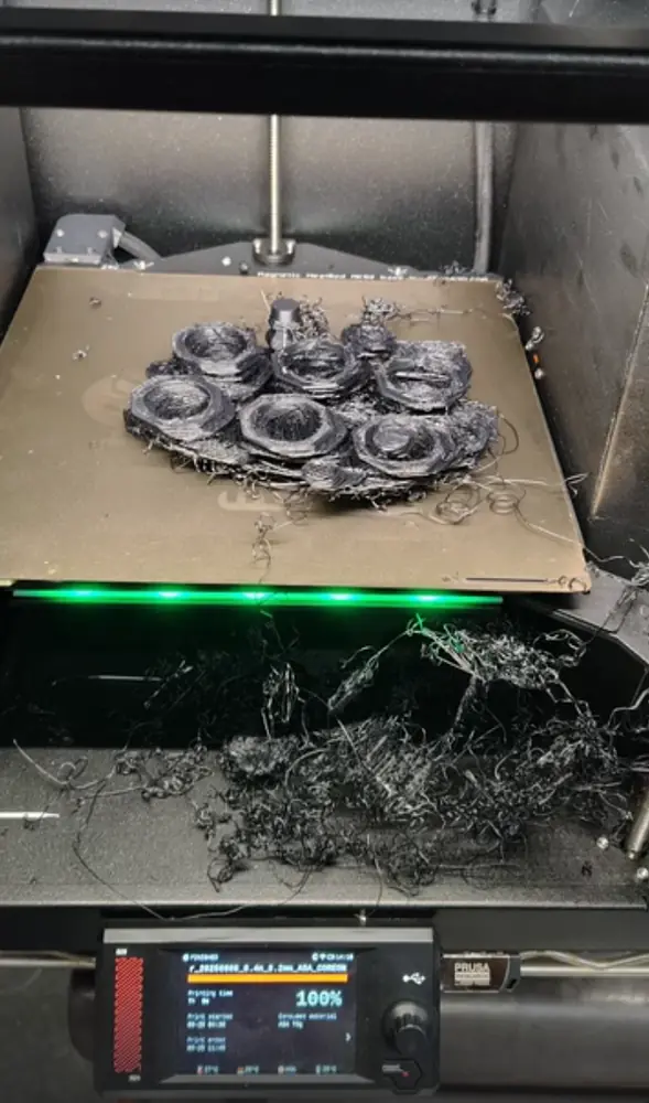 3D printer bed covered in a tangle of failed black filament after a print gone wrong