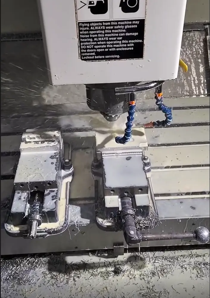 CNC mill machining stainless steel between two vises, spraying coolant and chips