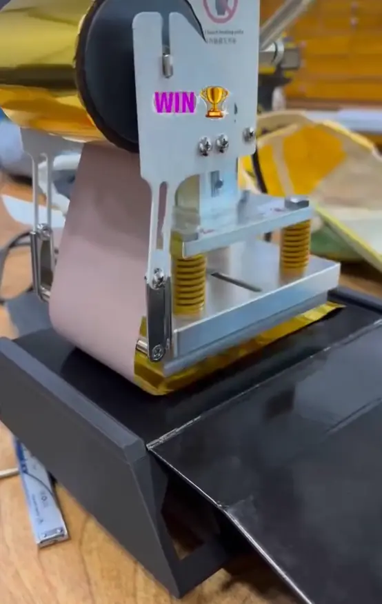 Foil-stamping press applying gold foil to a black NEUTRINO box, captioned “WIN”